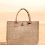 Earth Tote eco-friendly jute tote bag with button detail, displayed on sand against a desert background